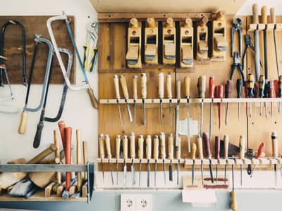 Eine gut organisierte Werkbank mit zahlreichen Handwerkzeugen hängt an einer Wand. Zu sehen sind Hobel, Feilen, Sägen und Schraubendreher, ordentlich aufgereiht an Haken und in Halterungen