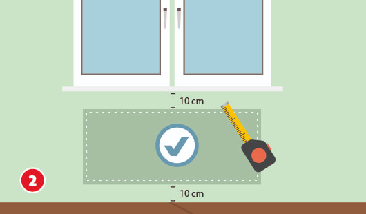 Eine schematische Darstellung zeigt die Auswahl des richtigen Standorts für einen Heizkörper unter einem Fenster. Ein Maßband markiert einen Bereich mit jeweils 10 cm Abstand zum Fensterbrett und zum Boden. Ein Häkchensymbol kennzeichnet den optimalen Montagebereich. Unten links ist ein roter Kreis mit einer weißen 2