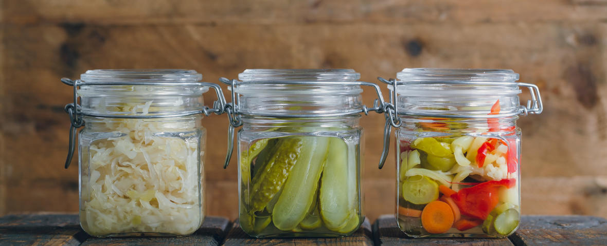 Drei Einmachgläser auf einem Holztisch, gefüllt mit Sauerkraut, Gewürzgurken und gemischtem eingelegtem Gemüse