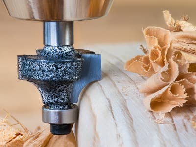 Ein Fräskopf bearbeitet die Kante eines Holzstücks und erzeugt dabei saubere Holzspäne. Die Konturfräse formt ein dekoratives Profil.