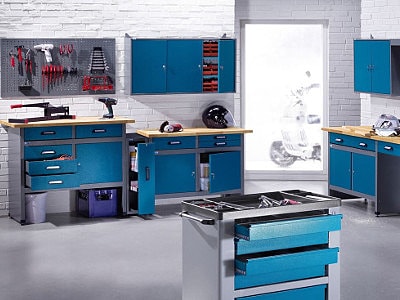 Eine modern eingerichtete Werkstatt mit blauen Werkbänken, Hängeschränken und einer Lochwand ist sauber und gut organisiert. Werkzeuge und Helme sind ordentlich verstaut.