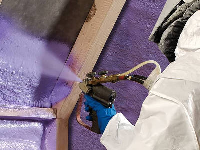 Eine Person im Schutzanzug sprüht violetten Dämmstoff auf eine Wandfläche