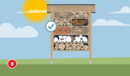 Eine schematische Darstellung zeigt das vollständig befüllte Insektenhotel mit verschiedenen Naturmaterialien in den einzelnen Fächern. Sichtbar sind Bambusrohre, gebohrte Holzscheiben, Stroh, Tannenzapfen, Schilfhalme, Tonziegel und weiße Steine. Die Materialien sind ordentlich sortiert und vollständig eingesetzt. Ein Häkchensymbol markiert die fachgerechte Befüllung. Unten links ist ein roter Kreis mit einer weißen 8