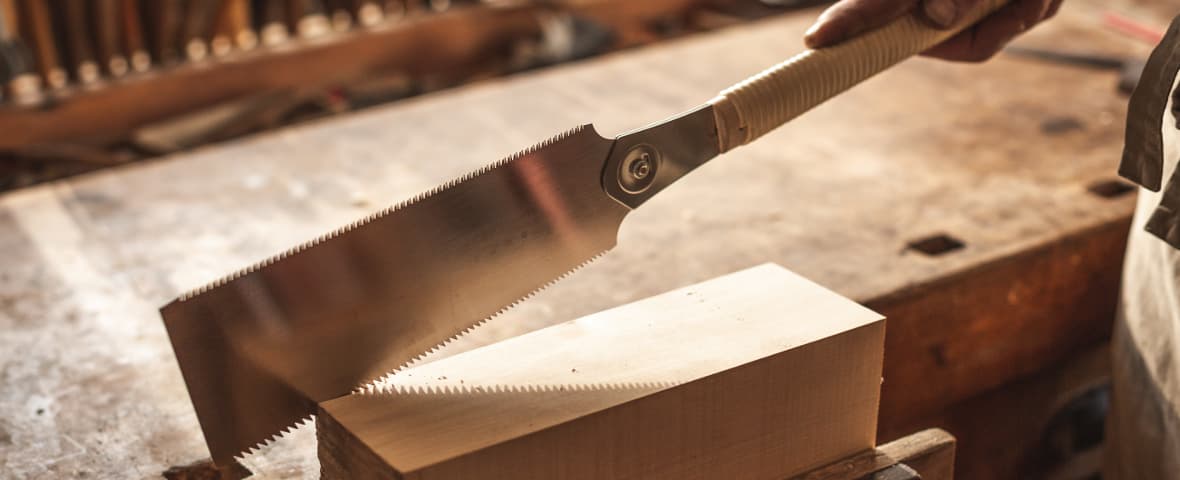 Eine feinzahnige Handsäge wird zum Schneiden eines Holzstücks angesetzt