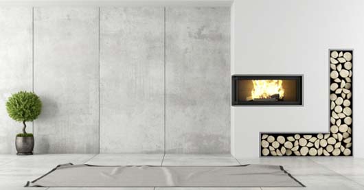 Minimalistisch gestaltetes Wohnzimmer mit wandintegriertem Kamin und sichtbarem Feuer. Rechts daneben ein L-förmiges Holzlager mit ordentlich gestapelten Scheiten. Links steht ein kleiner Kugelbuchsbaum in einem dunklen Topf