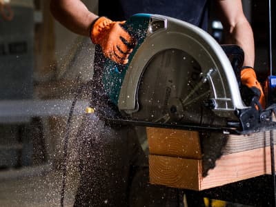 Eine Person schneidet mit einer Kreissäge ein Holzbrett, Holzspäne fliegen