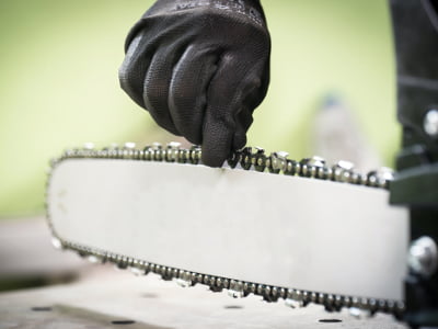 Eine Person prüft mit Handschuhen die Kette einer Motorsäge