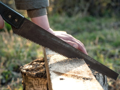 Eine Person sägt mit einer Handsäge ein Holzbrett im Freien
