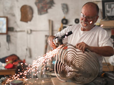 Ein Mann schleift eine Metallskulptur mit einem Winkelschleifer, dabei fliegen Funken