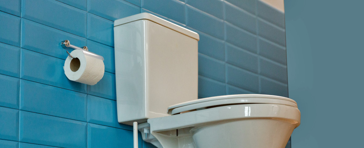 Bild einer Toilette mit weißem Spülkasten an einer blau gefliesten Wand