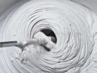 Ein Rührwerk vermischt weißen Putz oder Spachtelmasse in einem Eimer. Die Masse bildet dabei eine spiralförmige Bewegung.