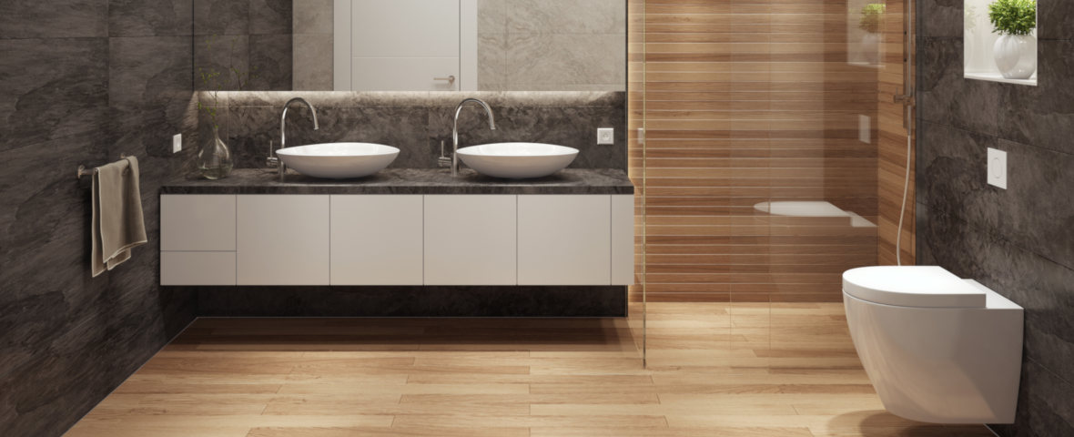 Ein modernes Badezimmer mit fertig installiertem Wand-WC, begehbarer Dusche mit Glaswand, zwei Waschbecken auf einer durchgehenden Waschtischplatte und stilvollen Wand- und Bodenfliesen in Holz- und Steinoptik. Das wandhängende WC befindet sich rechts im Raum, elegant montiert mit flacher Betätigungsplatte oberhalb