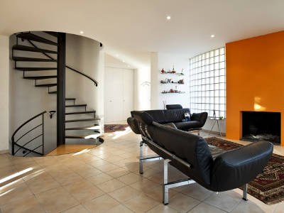 Wohnzimmer mit schwarzer Wendeltreppe, modernen Ledersofas und orangefarbener Wand mit Kamin