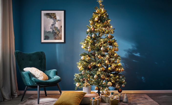 Eingeschmückter Weihnachtsbaum steht in einem Wohnzimmer vor einer blauen gestrichenen Wand