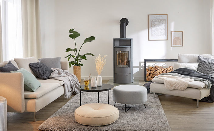 Helles Wohnzimmer mit Kaminofen, gemütlicher Sitzecke, Holzlager im Metallregal und moderner Dekoration.