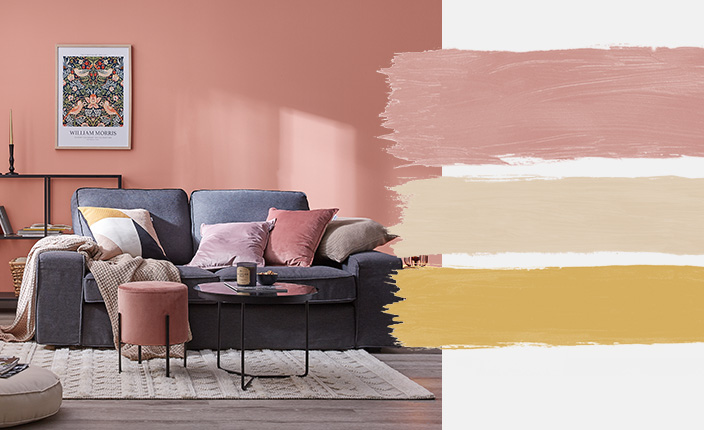 Ein stilvoll eingerichtetes Wohnzimmer mit roséfarbener Wand und dunkelblauem Sofa, ergänzt durch pastellfarbene Kissen. Rechts davon die Farbtöne der Palette „Crystal Rose“ in Rosa, Beige und Senfgelb