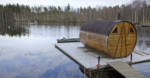 Fasssauna auf einem schwimmenden Steg an einem See im Wald.