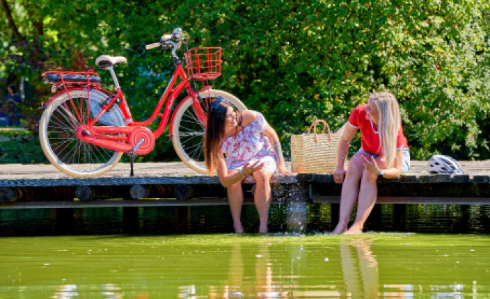 Zwei Frauen sind am Wasser mit einem Roten Fahrrad im Hintergrund