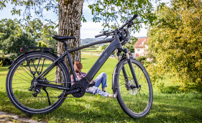 Ein Mann schläft an einem Baum mit einem Fahrrad von Fischer im Vordergrund