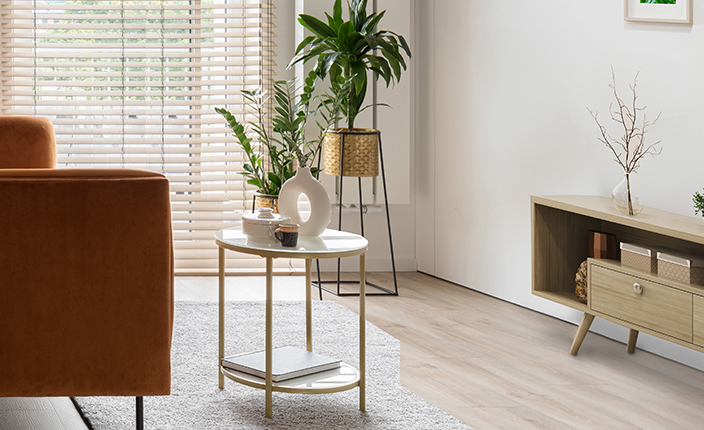 Ein stilvoll eingerichteter kleiner Wohnraum mit hellen Farben, minimalistischer Einrichtung und viel Tageslicht. Ein runder Beistelltisch, Zimmerpflanzen und ein helles Sideboard sind zu sehen