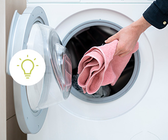 Hand steckt rosa Handtuch in die Trommel einer Frontlader-Waschmaschine. Rechts im Bild steht in grün: „ENERGIESPARTIPPS ZUM STROM SPAREN“. Darunter in schwarz: „Wir zeigen Dir die größten Stromfresser in Deinem Haushalt.“ Unten rechts befindet sich ein grüner Button mit weißer Schrift: „JETZT ENTDECKEN“.