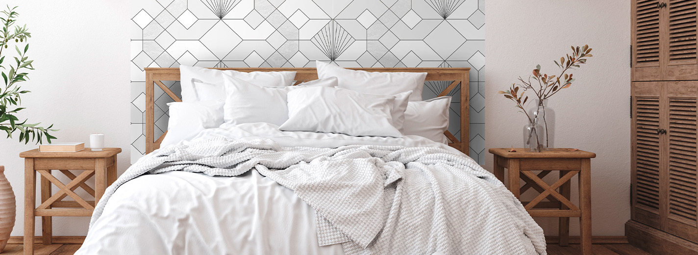 Schlafzimmer mit weißem Bett, geometrischer Tapete in Schwarz-Weiß als Wandakzent und zwei Nachttischen aus Holz mit Dekoobjekten.