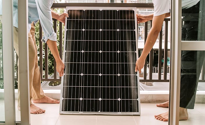 Zwei Personen montieren barfuß ein Balkonkraftwerk mit Solarpanel auf einem Balkon.
