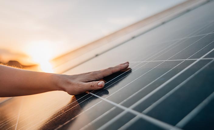 Eine Hand berührt bei Sonnenuntergang ein Solarpanel.