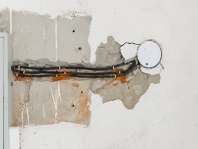 Foto einer geöffneten Wand mit freigelegten Elektroleitungen, die zu einer Unterputzdose verlaufen, der Untergrund der Wand wirkt nass
