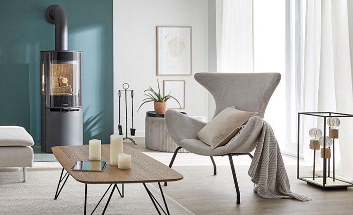 Helles Wohnzimmer mit moderner Einrichtung, skandinavischem Sessel, Holzofen, Dekokerzen und stilvoller Stehleuchte in schwarzem Metallrahmen.