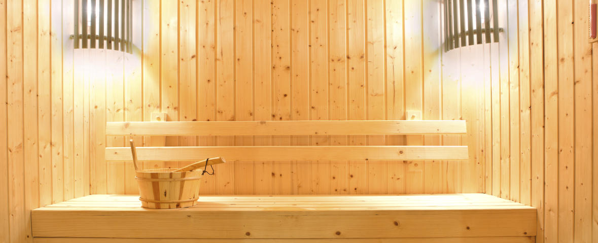 Holzsauna mit Bank, Aufgusseimer und zwei Wandlampen.