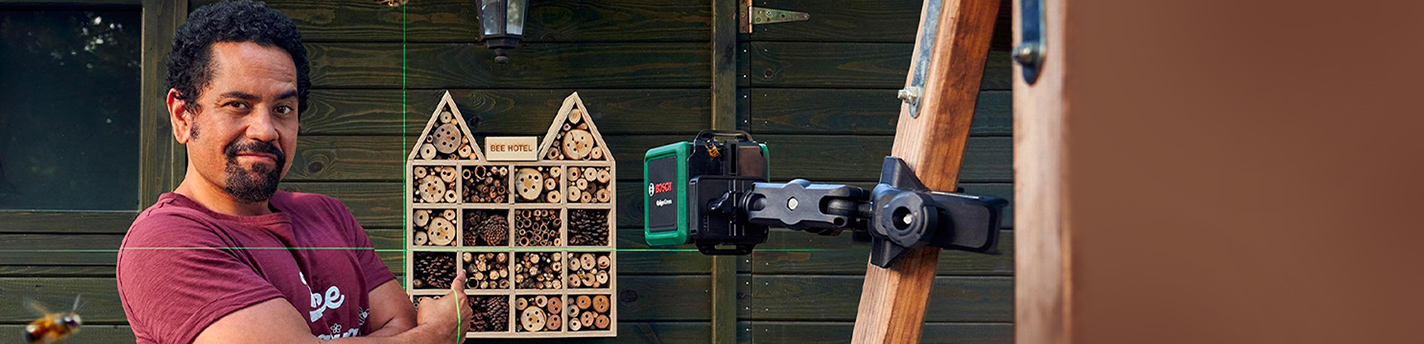 Eine Abbildung von einem Mann der Bosch Messtechnikverwendet um ein Insektenhotelaufzuhängen an einem Holzschuppen