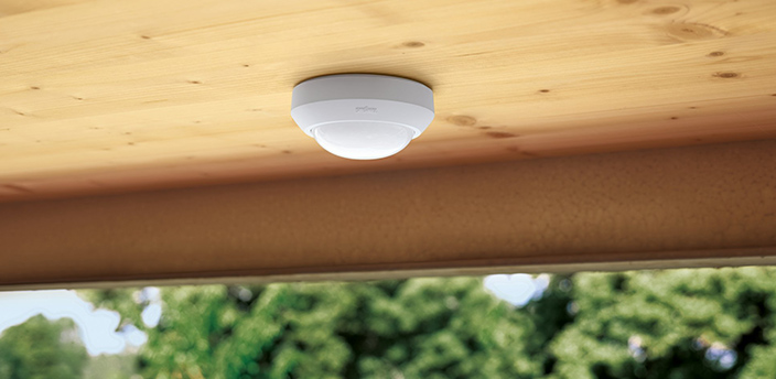 Bewegungsmelder an einer Holzdecke im Außenbereich zur automatischen Lichtsteuerung.