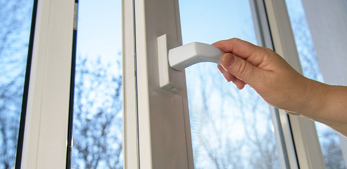 Hand öffnet den Griff eines modernen 3-fach verglasten Fensters.