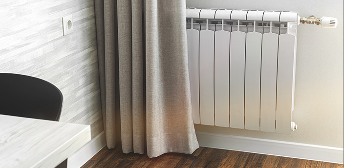 Weißer Heizkörper teilweise von einem Vorhang verdeckt.