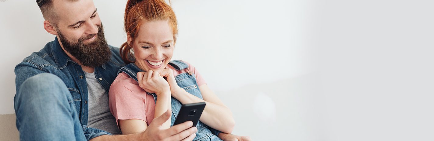 Eine Frau und ein Mann sitzen mit dem Rücken an einer Wand und schauen gemeinsam auf ein Tablet