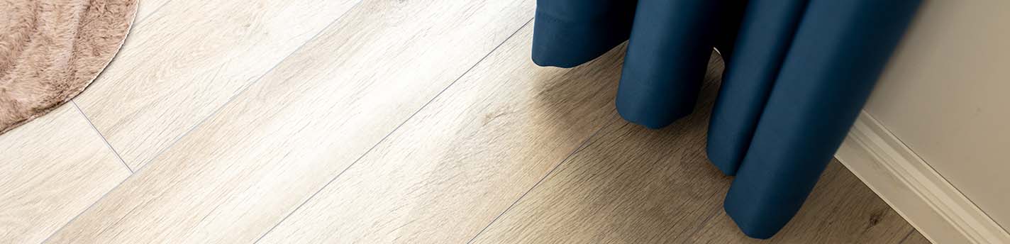 Heller Holzfußboden mit blauem Vorhang und einem Ausschnitt eines beigen Teppichs.