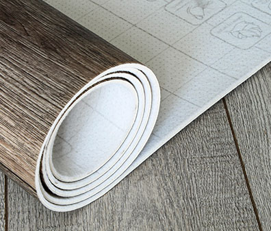 Aufgerollter Vinylboden in Holzoptik auf grauem Holzboden.