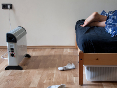 Ein Konvektor-Heizgerät steht neben einem Bett in einem Schlafzimmer mit Holzfußboden, während eine Person darin liegt