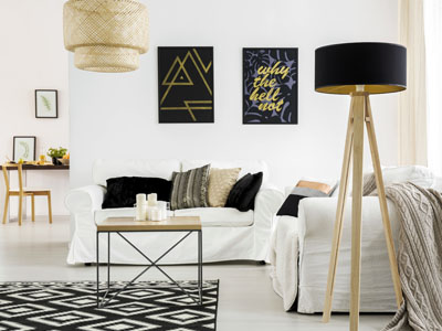 in modern eingerichtetes Wohnzimmer zeigt zwei weiße Sofas mit Kissen, einen Couchtisch, eine Stehlampe und Wandbilder in Schwarz-Gold. Ein schwarz-weiß gemusterter Teppich liegt auf dem Boden.