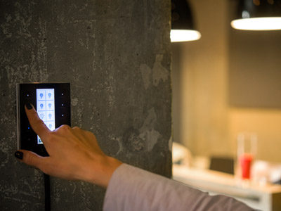 Eine Person bedient ein modernes Touchpanel zur Lichtsteuerung an einer Betonwand in einem Wohnraum