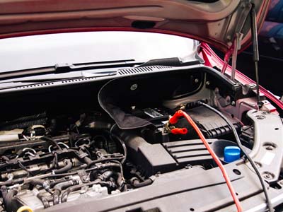 Detailaufnahme eines geöffneten Motorraums eines Autos mit angeschlossenem Starthilfekabel an der Autobatterie