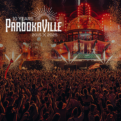 Eine große Menschenmenge feiert auf dem PAROOKAVILLE-Festival vor einer Bühne mit vielen roten Lichtern und Feuerwerk.