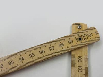 Ein Zollstock aus Holz liegt aufgeklappt auf einer weißen Fläche. Die Skala ist gut lesbar und zeigt einen Bereich um die 100-Zentimeter-Marke