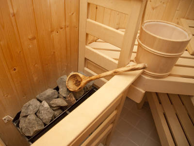 Saunaofen mit Steinen, Holzeimer und Schöpfkelle in einer Holzsauna.