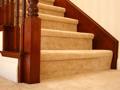 Eine Treppe mit beigem Teppichboden führt nach oben. Das Geländer besteht aus dunkelbraunem Holz mit gedrechselten Stäben.
